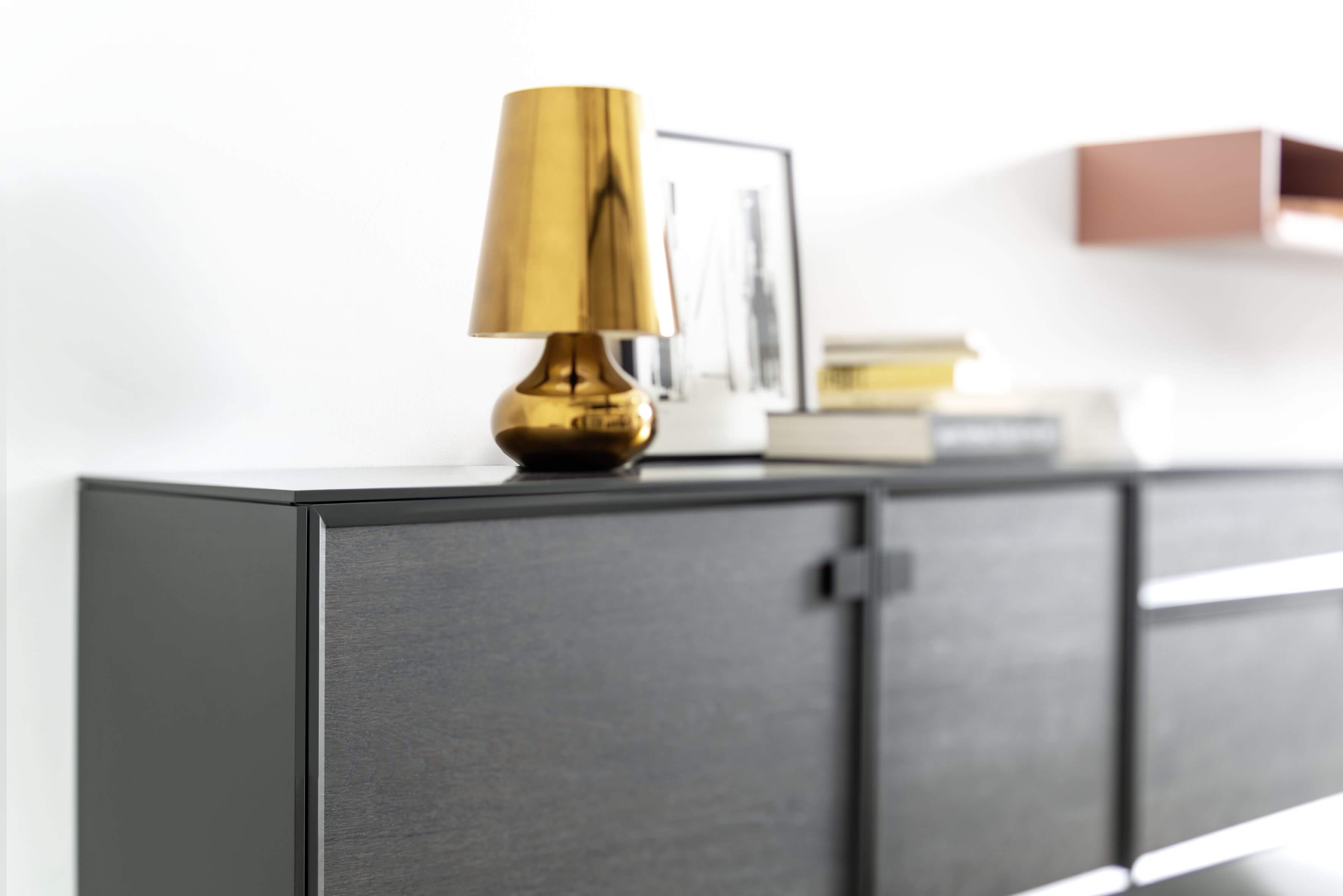 Graues Sideboard mit einer goldenen Lampe und weiterer minimalistischer Dekoration.